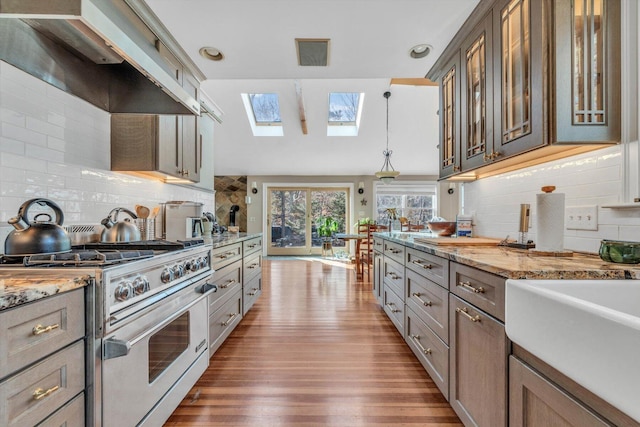 13 Try Works Rd, Truro, MA 02666 - kitchen with stainless steel stove, wall chimney range hood, a skylight, wood finished floors, and decorative backsplash