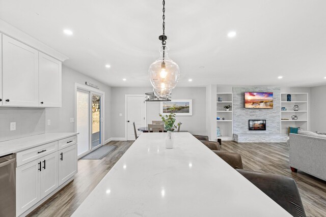 kitchen featuring a fireplace, white cabinetry, hanging light fixtures, stainless steel dishwasher, and light stone counters