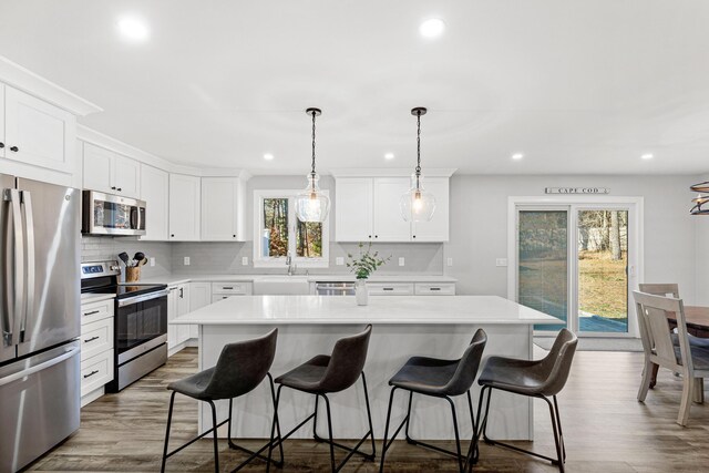 kitchen with decorative light fixtures, white cabinetry, appliances with stainless steel finishes, and a center island