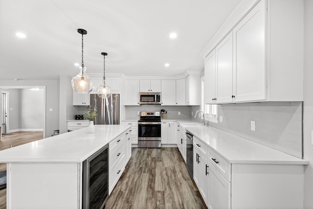 kitchen featuring hanging light fixtures, white cabinetry, a center island, beverage cooler, and stainless steel appliances