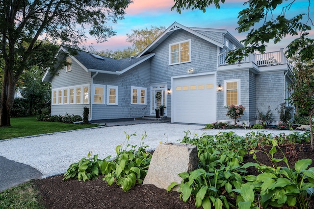 shingle-style home featuring an attached garage, a yard, gravel driveway, and a balcony