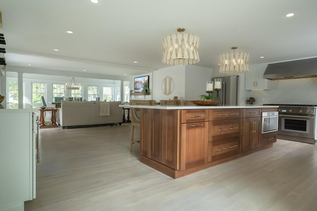 kitchen with wall oven, wall chimney exhaust hood, open floor plan, an inviting chandelier, and light countertops