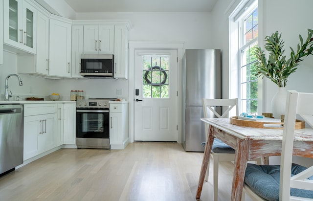 kitchen with light wood finished floors, appliances with stainless steel finishes, glass insert cabinets, and white cabinets