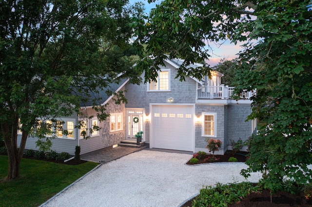 view of front of house featuring gravel driveway, a balcony, a garage, and a yard