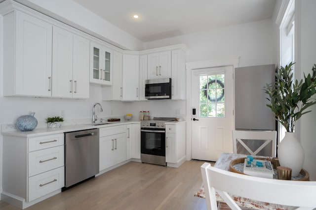 kitchen featuring light wood finished floors, light countertops, appliances with stainless steel finishes, white cabinets, and a sink