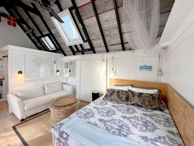 bedroom with hardwood / wood-style floors, wooden walls, high vaulted ceiling, and a skylight