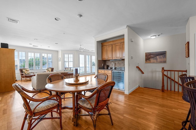 dining area with wine cooler, ceiling fan, a wealth of natural light, and light wood-type flooring