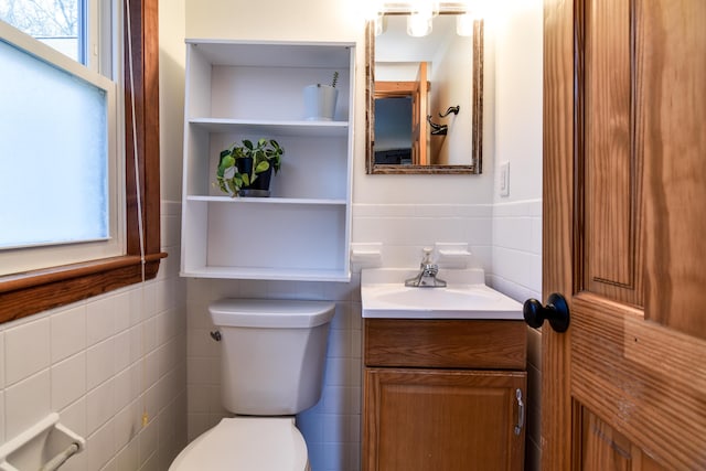 half bath featuring tile walls, toilet, vanity, and wainscoting