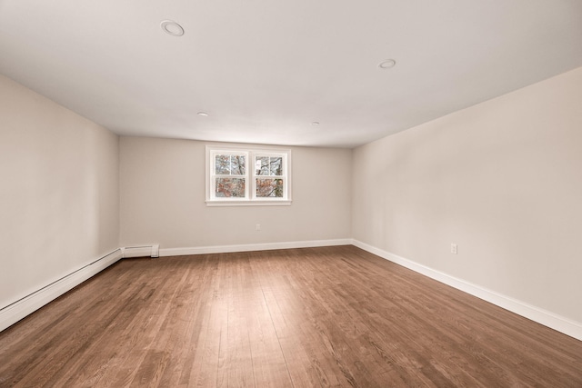 empty room featuring baseboard heating and hardwood / wood-style flooring