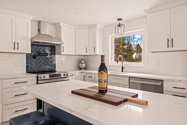 kitchen featuring white cabinetry, wall chimney range hood, stainless steel appliances, tasteful backsplash, and hanging light fixtures