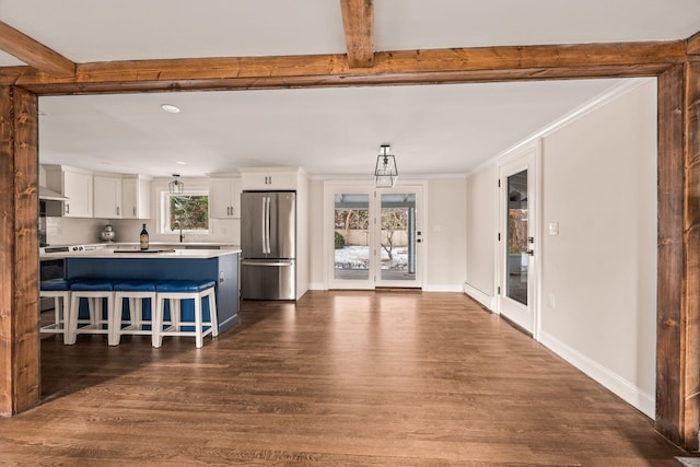 kitchen featuring crown molding, pendant lighting, stainless steel fridge, white cabinetry, and a breakfast bar area