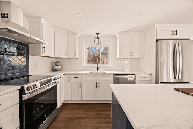 kitchen with appliances with stainless steel finishes, wall chimney range hood, sink, white cabinets, and pendant lighting