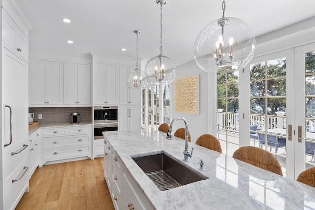 kitchen with light stone countertops, sink, white cabinetry, and an inviting chandelier