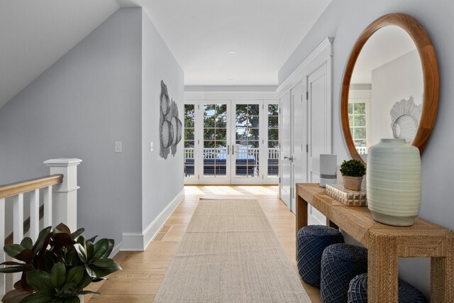 corridor with french doors, light hardwood / wood-style floors, and lofted ceiling