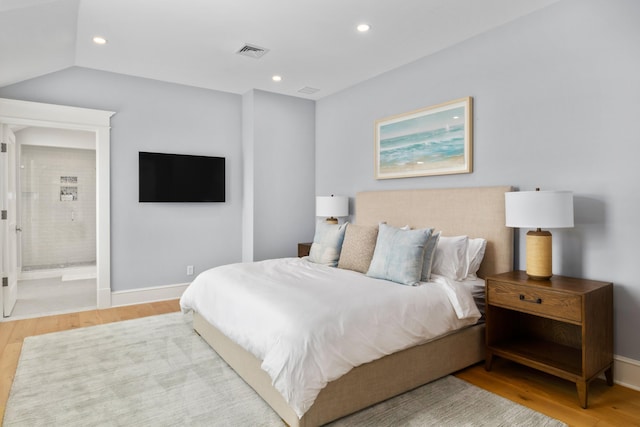 bedroom featuring hardwood / wood-style floors, ensuite bath, and vaulted ceiling