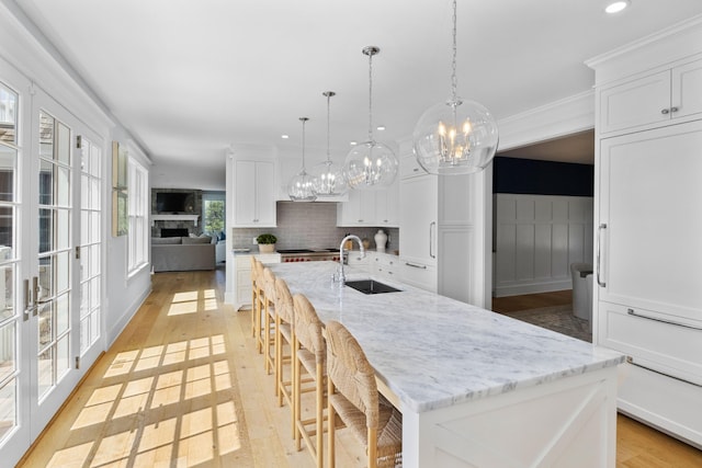 kitchen featuring sink, decorative light fixtures, white cabinetry, and a large island with sink