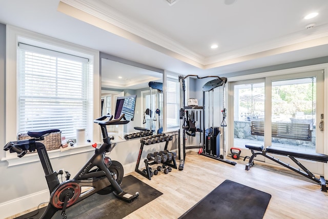 exercise room featuring ornamental molding, light hardwood / wood-style flooring, and a raised ceiling