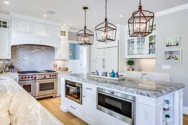 kitchen with decorative light fixtures, white cabinets, appliances with stainless steel finishes, and light stone countertops