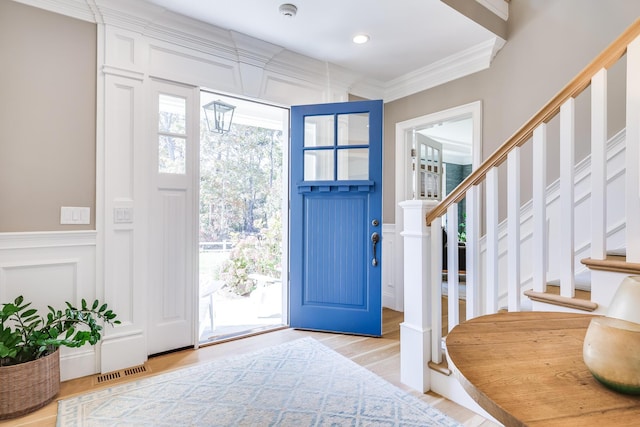 entryway featuring a decorative wall, stairs, ornamental molding, light wood-style flooring, and a wainscoted wall