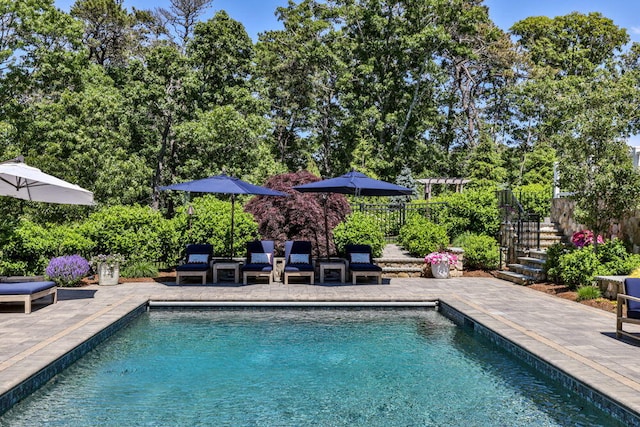 view of pool with a patio area, fence, view of wooded area, and stairway