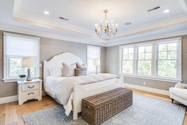 bedroom featuring light hardwood / wood-style floors, a raised ceiling, crown molding, and an inviting chandelier