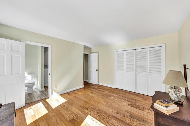 unfurnished bedroom featuring a closet, connected bathroom, baseboards, and wood finished floors