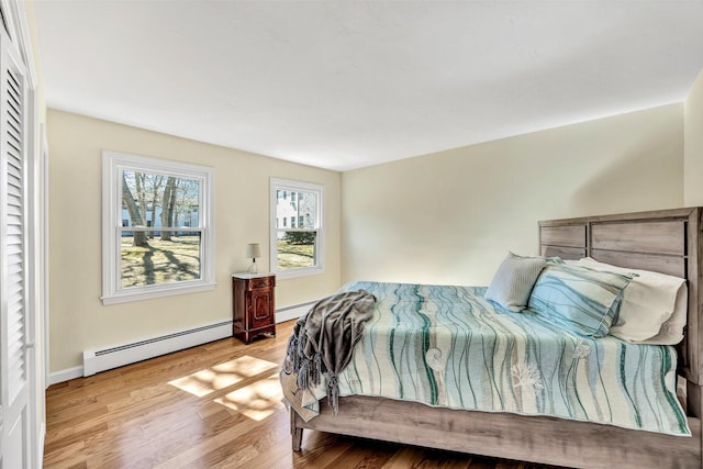 bedroom featuring a baseboard heating unit, baseboards, and wood finished floors