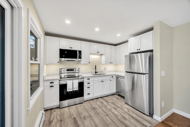 kitchen with light wood-type flooring, light countertops, appliances with stainless steel finishes, white cabinetry, and a sink