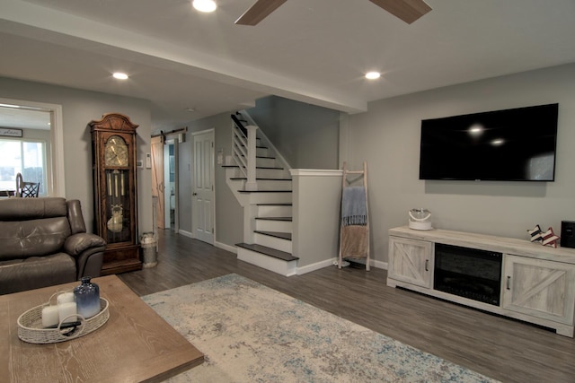 living area featuring baseboards, ceiling fan, stairs, dark wood-type flooring, and a barn door