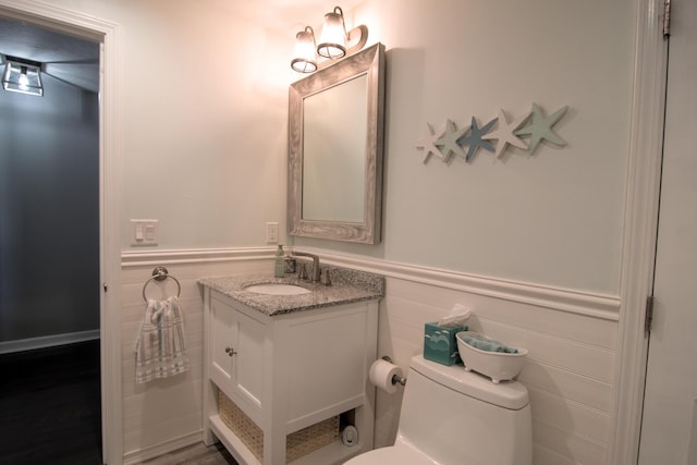 half bath featuring vanity, toilet, and wainscoting