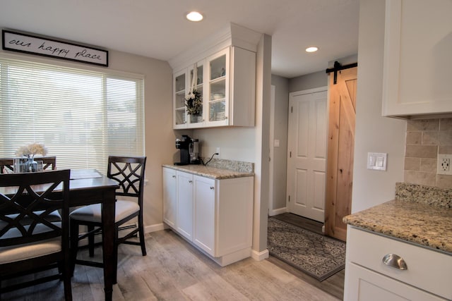 kitchen featuring white cabinetry, a barn door, light wood-style flooring, and decorative backsplash