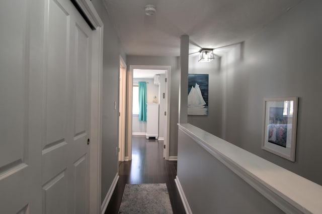 hall featuring an upstairs landing, dark wood-style flooring, and baseboards