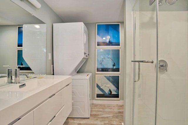 bathroom featuring wood-type flooring, a shower with shower door, stacked washer / drying machine, and vanity