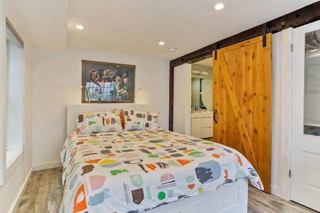 bedroom featuring connected bathroom, a barn door, and light hardwood / wood-style floors