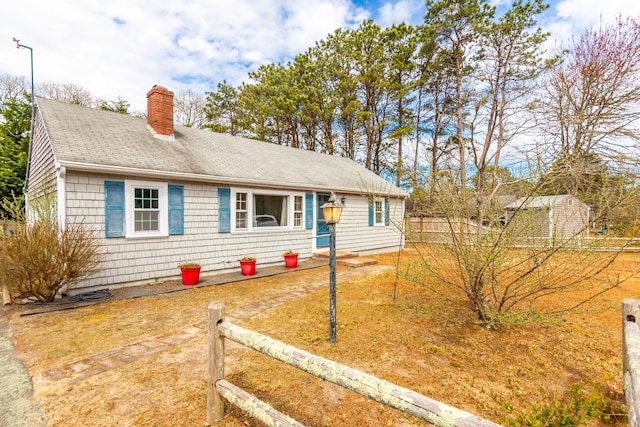 ranch-style home with a chimney, a shingled roof, and fence
