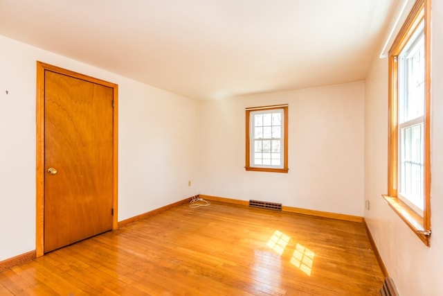 empty room with light wood-style floors, visible vents, and baseboards