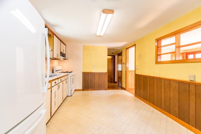 kitchen featuring light countertops, wood walls, wainscoting, and white appliances
