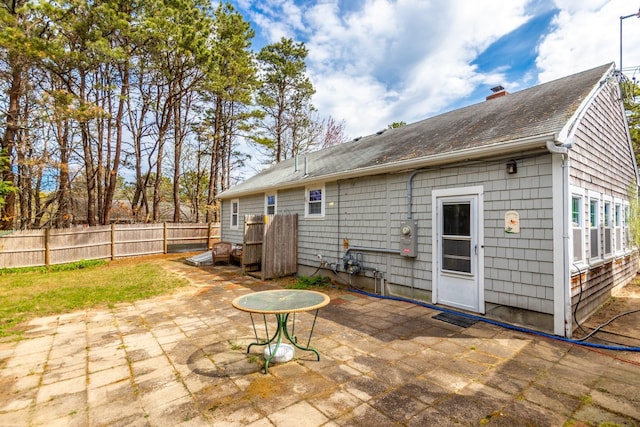 rear view of property featuring a chimney, a patio, a shingled roof, and fence