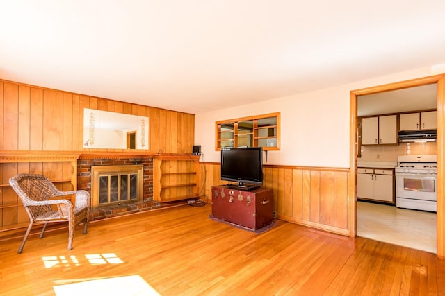 living room with wainscoting, light wood finished floors, wooden walls, and a brick fireplace