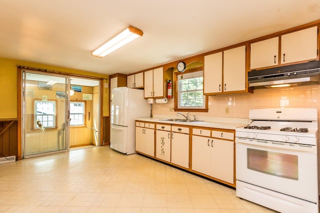 kitchen featuring a sink, white appliances, backsplash, under cabinet range hood, and light countertops