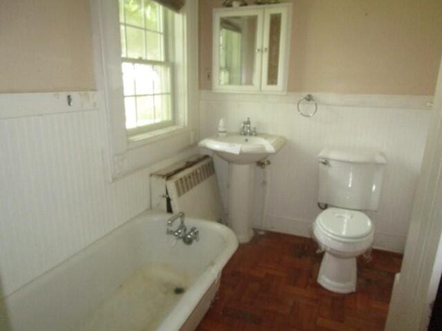 bathroom with radiator heating unit, a bath, toilet, and parquet flooring