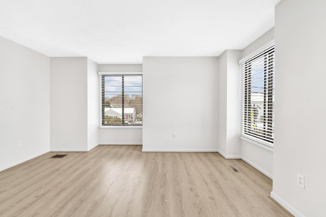 empty room with visible vents, a healthy amount of sunlight, and wood finished floors