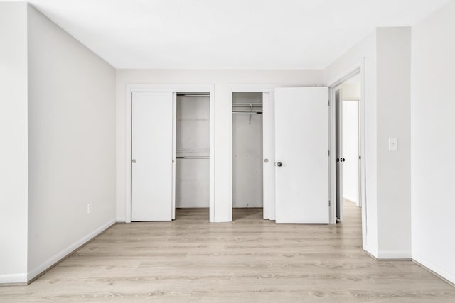 unfurnished bedroom with light wood-style flooring, two closets, and baseboards