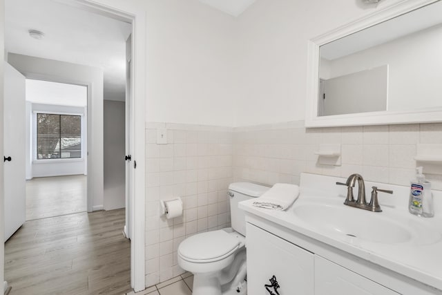 bathroom featuring tile walls, a wainscoted wall, toilet, wood finished floors, and vanity