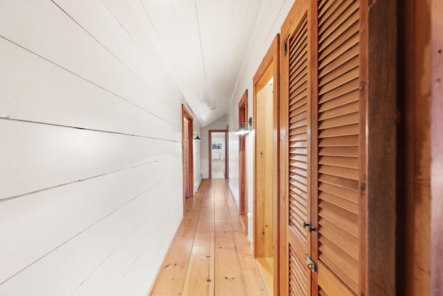 corridor with wooden walls, light hardwood / wood-style flooring, and vaulted ceiling