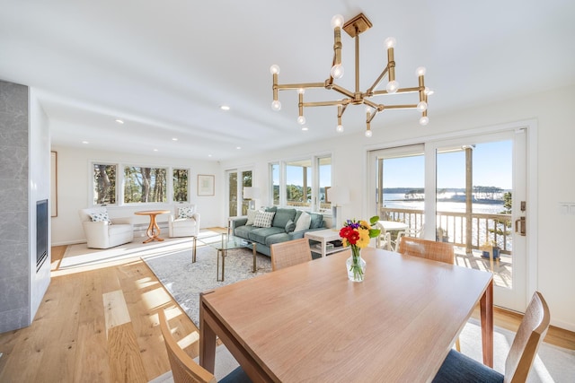 dining room with a fireplace, light wood-type flooring, a water view, and an inviting chandelier