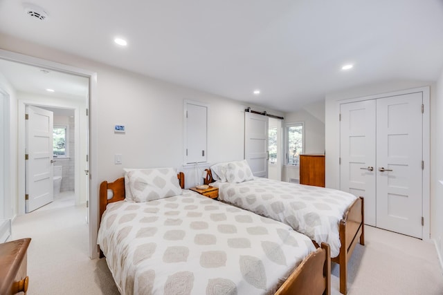 bedroom with light colored carpet, a closet, ensuite bath, and a barn door