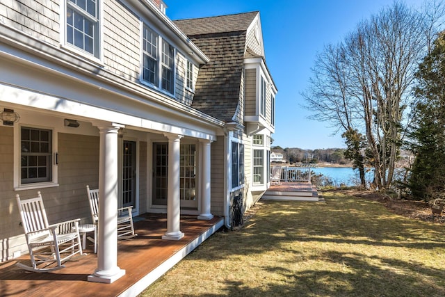 exterior space with a lawn, roof with shingles, a water view, and a gambrel roof