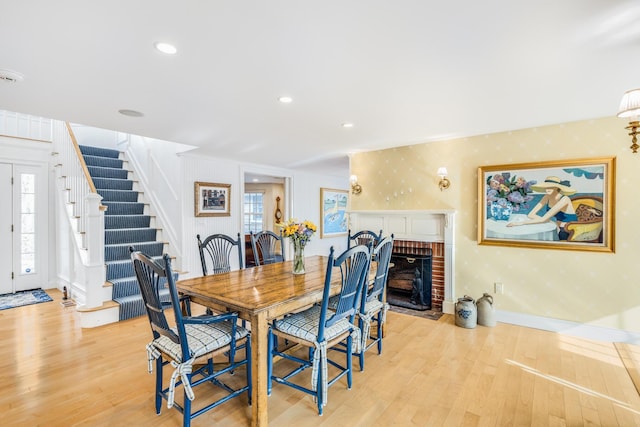 dining area with light wood-type flooring, a healthy amount of sunlight, a fireplace, and stairway