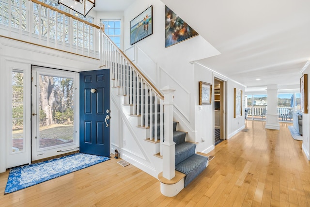 foyer entrance featuring decorative columns, visible vents, stairway, hardwood / wood-style floors, and a high ceiling